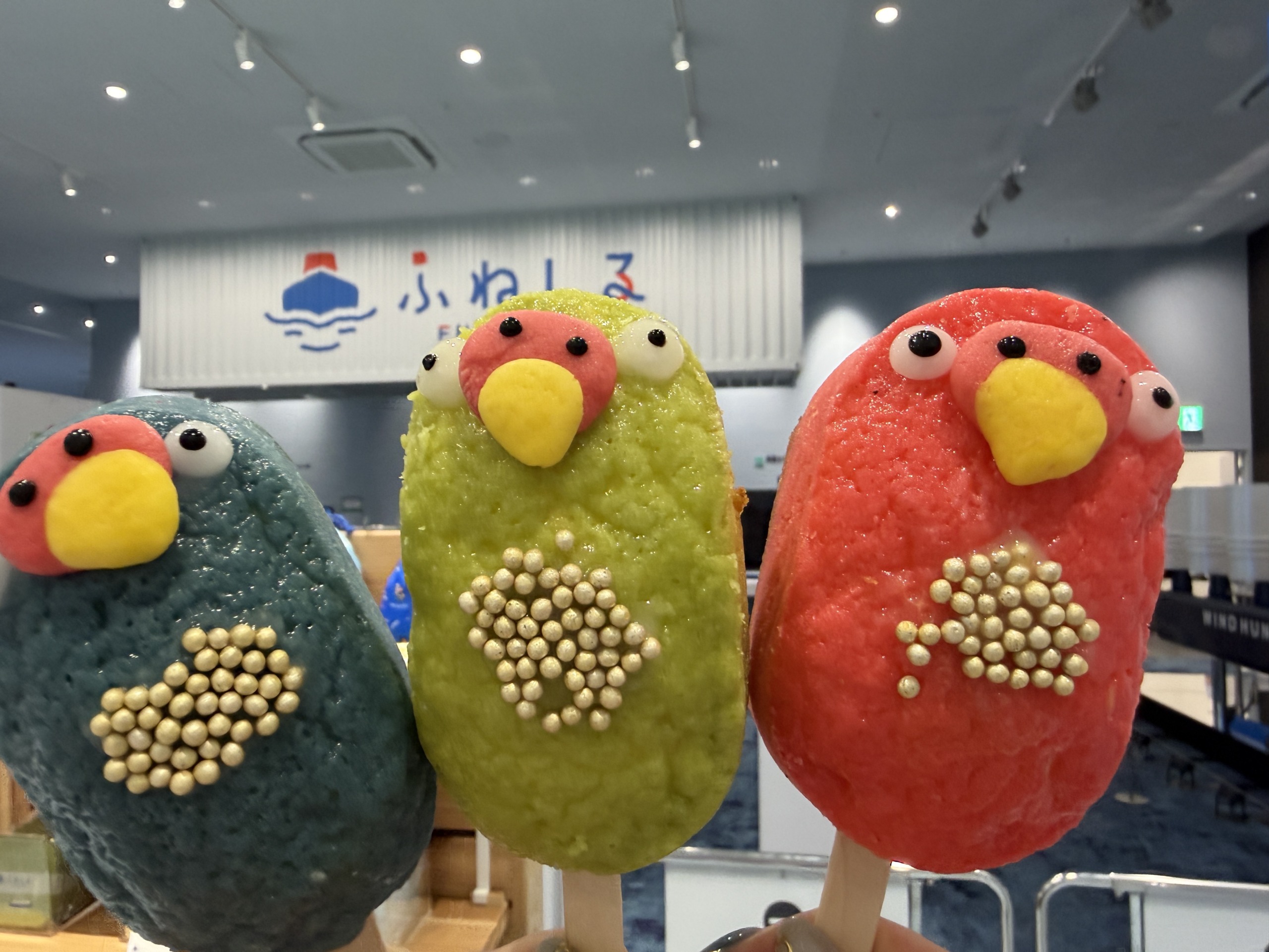 手に持った、鳥の形をした三色のスイーツのクローズアップ